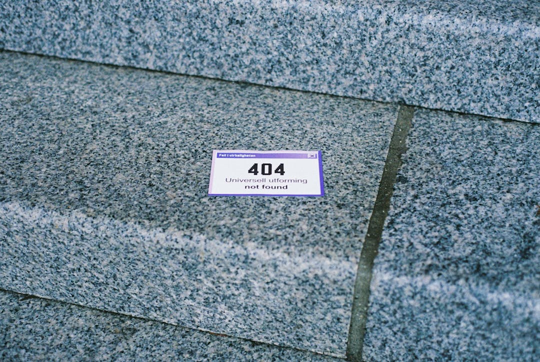 Et klistremerke med teksten 404 Universell utforming not found er klistret på et trappetrinn i stein.