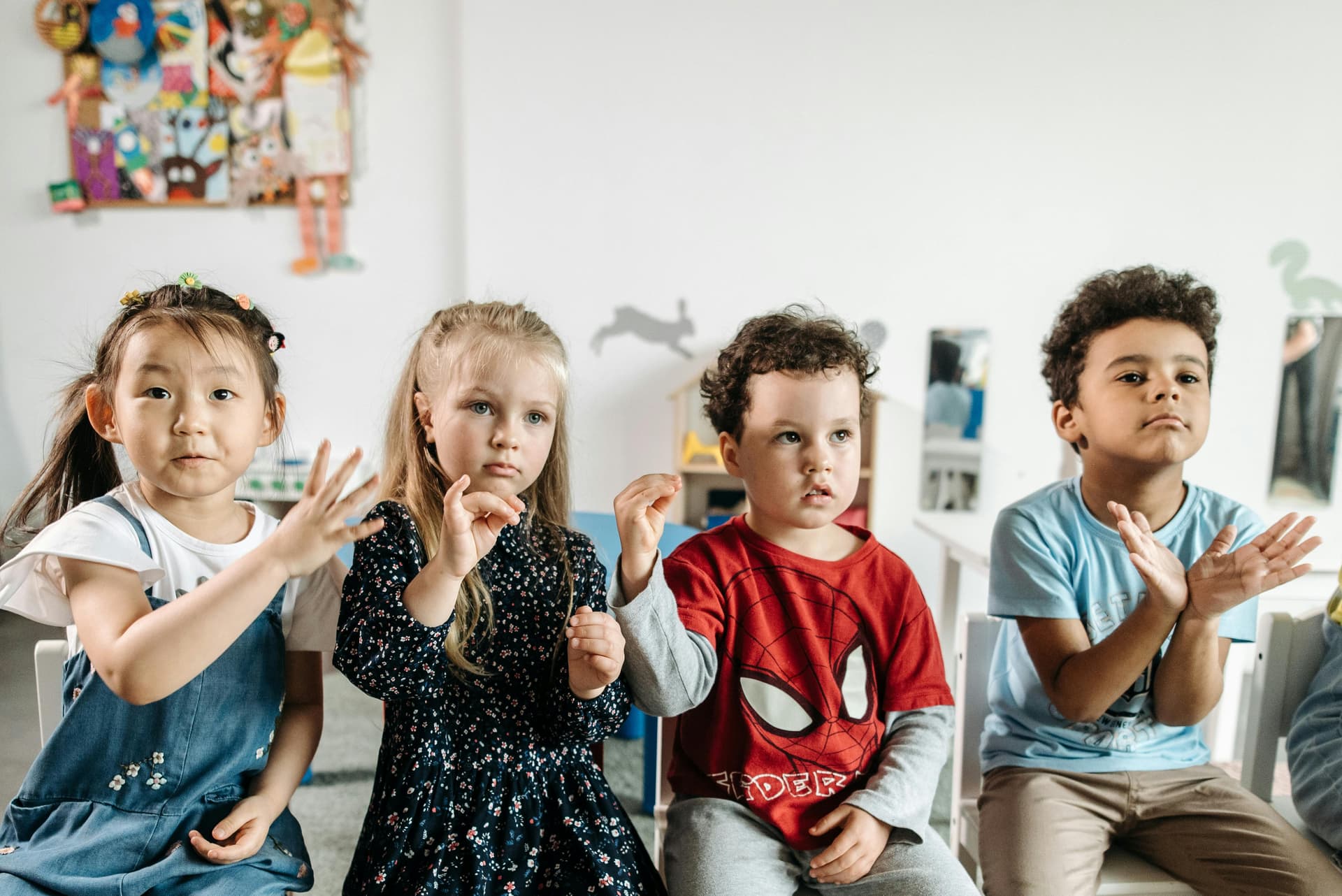 Fire barn sitter på rad og rekke i et klasserom. De øver på ulike tegnspråk.