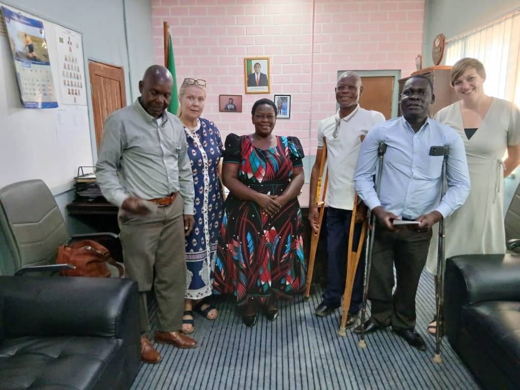 Flere mennesker står inne i et møterom. Noen går med krykker og andre står oppreist.