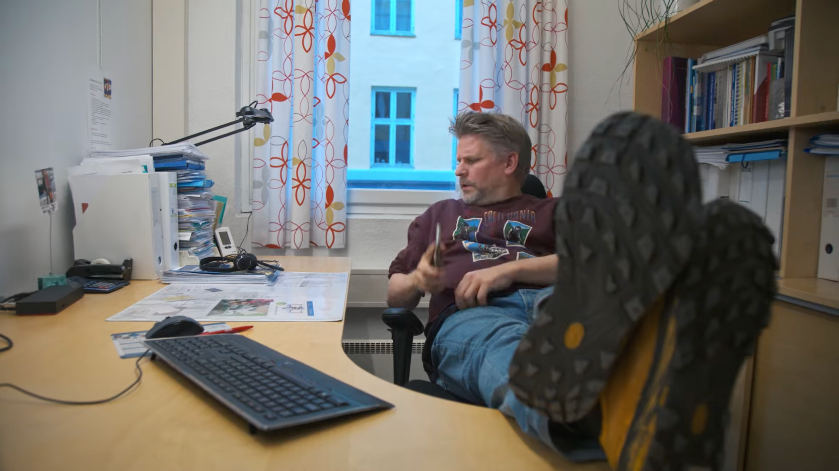 På et kontor sitter en mann med beina på bordet og ser ned på papirer.