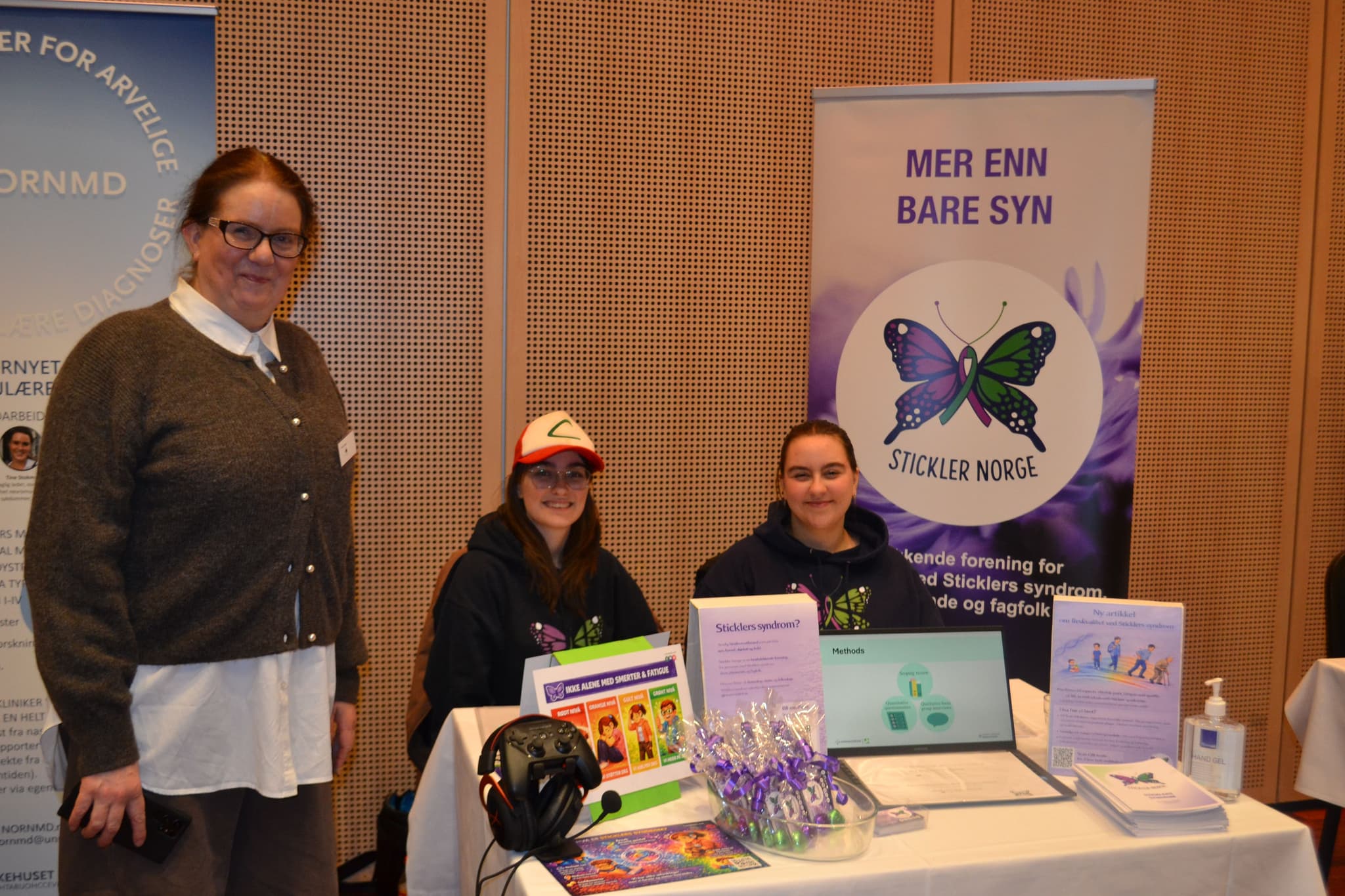 Tre personer er på plass i et minglerom på et hotell. De smiler til kamera. Foran seg har de brosjyrer og annet matriell.